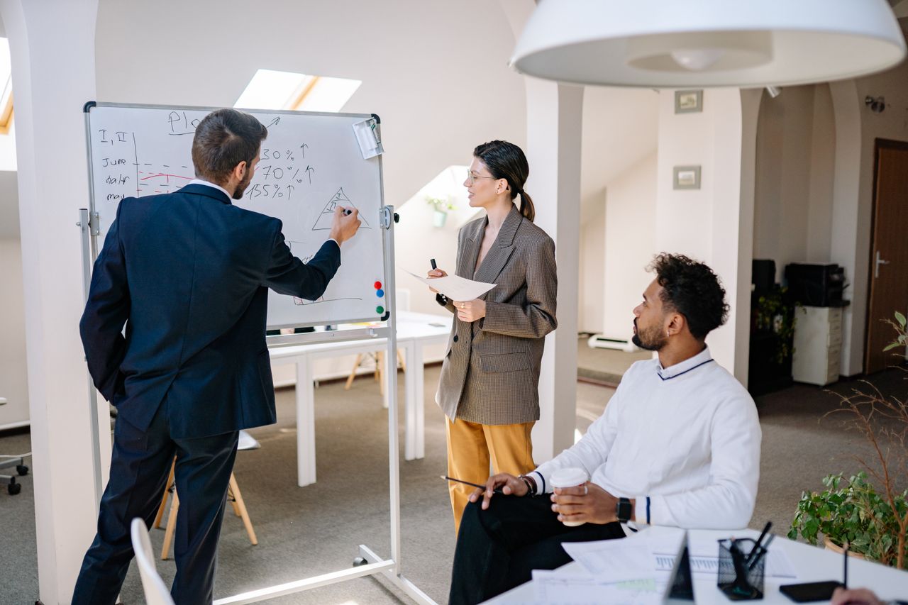 Diverse colleagues collaborating on a project using a whiteboard in a modern office setting.